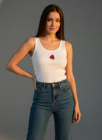 Woman wearing a white tank top with a watermelon design and blue jeans against a gray background