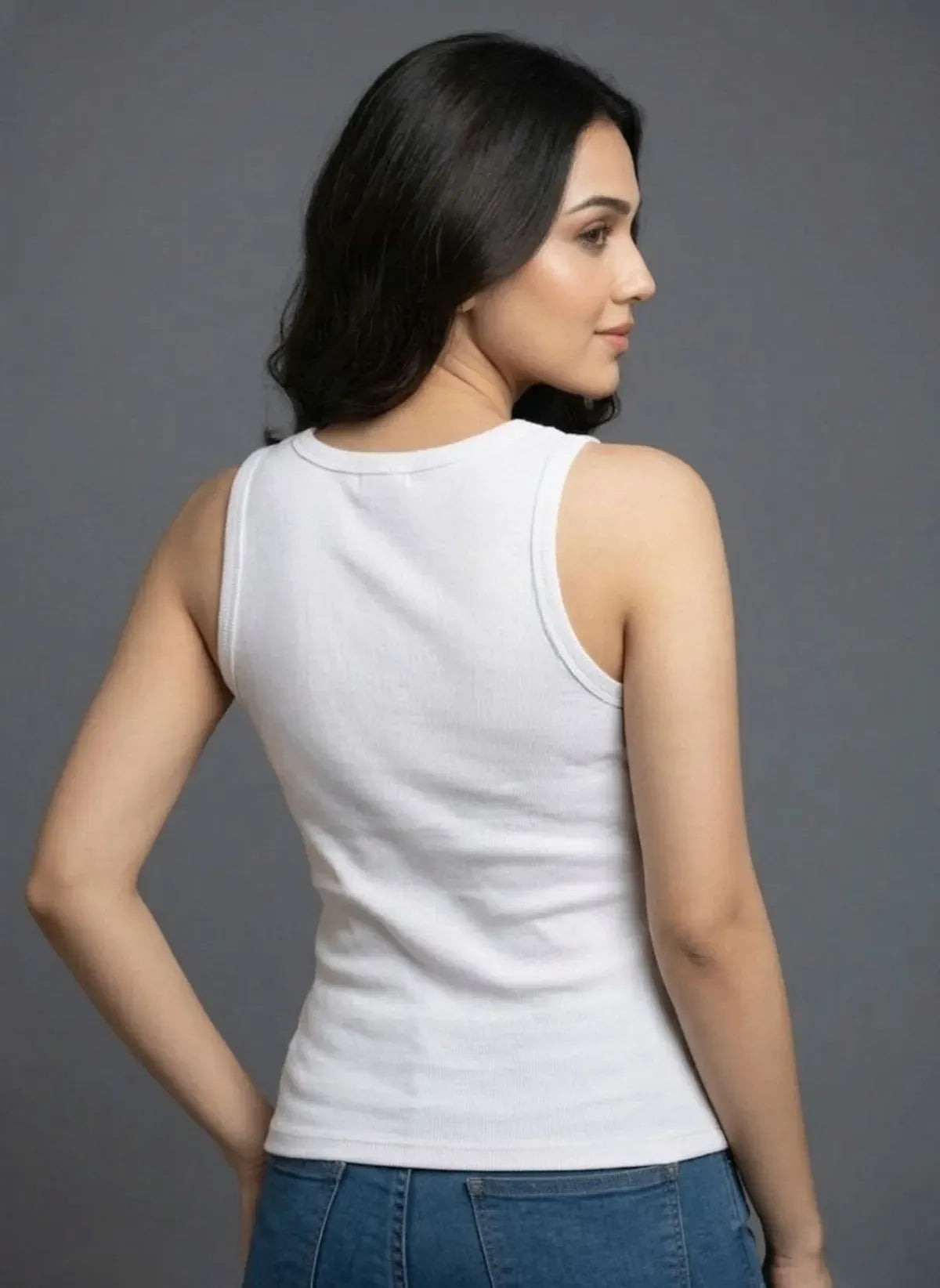 Woman wearing a white sleeveless top and blue jeans against a gray background